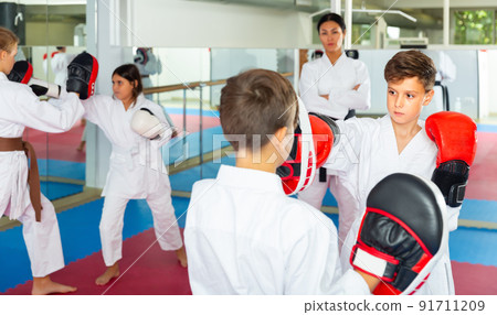 Two boys in boxing gloves launching blows during self defense workout in gym 91711209