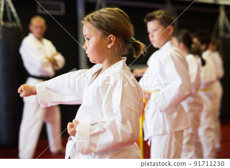 Kids in kimonos practicing karate techniques in group workout at training room Kids in kimonos practicing karate techniques in group workout at training room 91711230