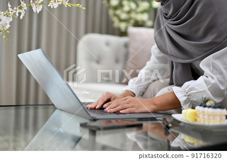 Muslim woman wearing hijab in the living room using laptop. cropped Muslim woman wearing hijab in the living room using laptop. cropped 91716320