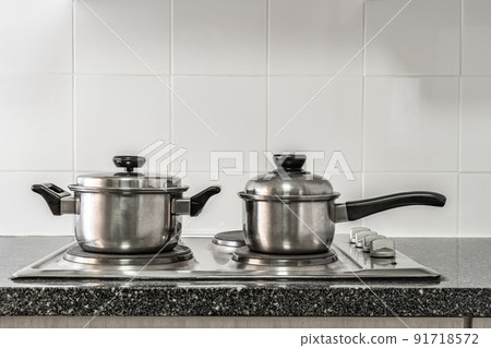 Couple of stainless pots on kitchen stove with marble counter top and white tile wall 91718572