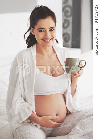Oh that glow. Shot of a pregnant woman relaxing with a beverage at home. 91718725