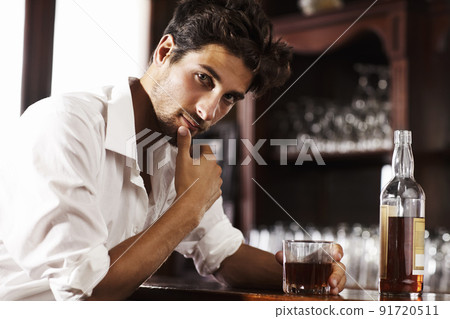 Gathering thoughts after a hectic day. Young sophisticated man drinking whiskey alone at the bar. Gathering thoughts after a hectic day. Young sophisticated man drinking whiskey alone at the bar. 91720511
