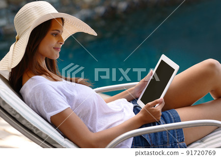 Doing some outdoor browsing. Shot of an attractive young woman using a digital tablet by the poolside. 91720769
