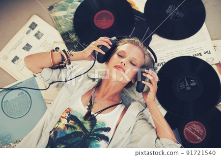 Keep calm and let the music play on. A young woman listening to music while lying on her back and surrounded by records. 91721540