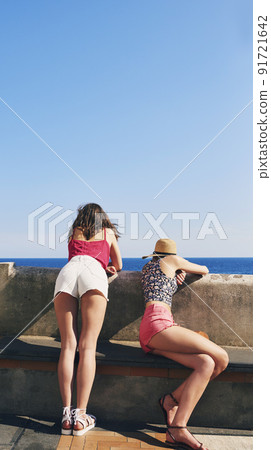 Two friends enjoying view of ocean in Italy. Rear view of fashion girl friends looking at view of sea on travel adventure vacation Two friends enjoying view of ocean in Italy. Rear view of fashion girl friends looking at view of sea on travel adventure vacation 91721642