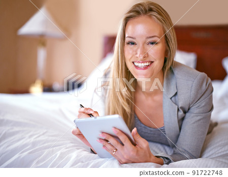 Loving the hotels wifi. A young businesswoman using a digital tablet in a bedroom. Loving the hotels wifi. A young businesswoman using a digital tablet in a bedroom. 91722748