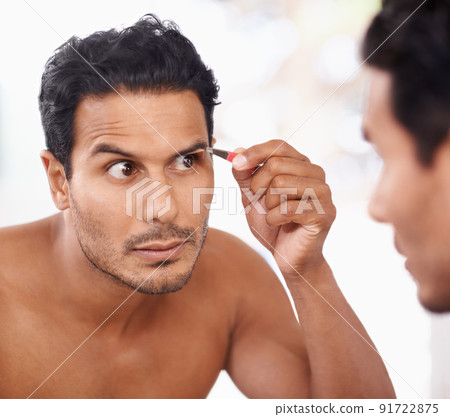He takes grooming to the next level. A young man plucking his eyebrows while looking in the mirror. 91722875