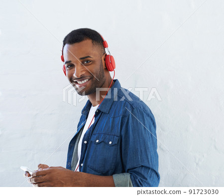 What an awesome track. A young african american man wearing a headphones and listening to music against a white background. 91723030