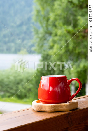Morning coffee in garden. Red mug on wooden board against blurred nature. 91724272