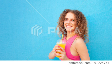 beautiful woman holds delicious orange juice, cold refreshing summer drink. Blue background, isolated. Outdoors, walk around city. Happy 91724735
