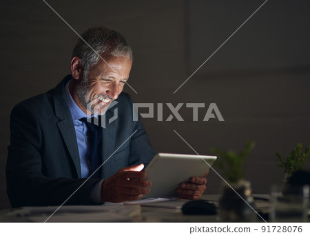 Working late made worthwhile. Shot of a mature businessman using a digital tablet while working late in an office. Working late made worthwhile. Shot of a mature businessman using a digital tablet while working late in an office. 91728076