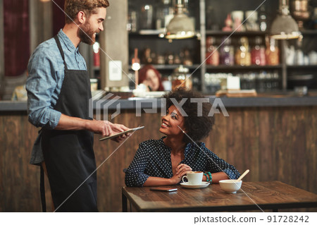 Would you like to hear about our specials. Shot of a young barista taking a customers order on a digital tablet at a cafe. Would you like to hear about our specials. Shot of a young barista taking a customers order on a digital tablet at a cafe. 91728242