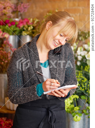 Business is blooming. Shot of a young woman taking an order at her florist shop. Business is blooming. Shot of a young woman taking an order at her florist shop. 91728404