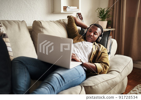 Let me open some of my oldest playlists.... Cropped shot of a handsome young man using a laptop while listening to music on his headphones in his living room at home. 91728534
