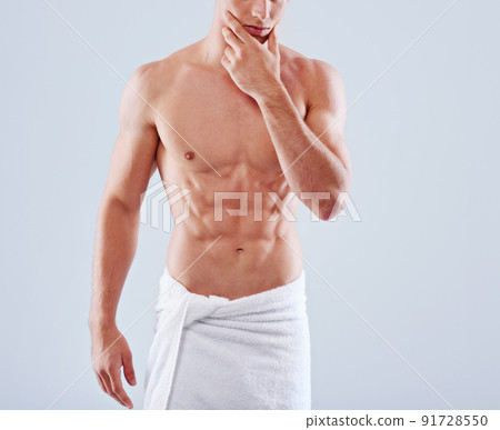 Abs-alicious. Cropped studio shot of a handsome bare chested young man with his waist wrapped in a towel. Abs-alicious. Cropped studio shot of a handsome bare chested young man with his waist wrapped in a towel. 91728550