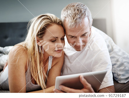 Lying in and watching our favorite tv series. Shot of a mature couple using a digital tablet while lying in bed. Lying in and watching our favorite tv series. Shot of a mature couple using a digital tablet while lying in bed. 91729187