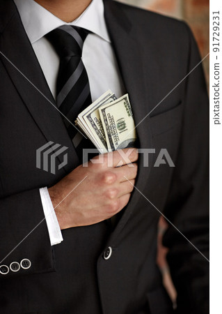 Hes not above accepting a bribe. Cropped shot of a man tucking a wad of cash into his jacket. 91729231