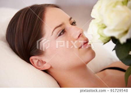 Her heart is won. A beautiful young woman lying down and admiring the bouquet of white roses she is holding. 91729548