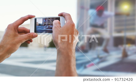 Capturing real life moments. Cropped shot of a man taking a picture of his friend doing tricks on his skateboard. 91732420
