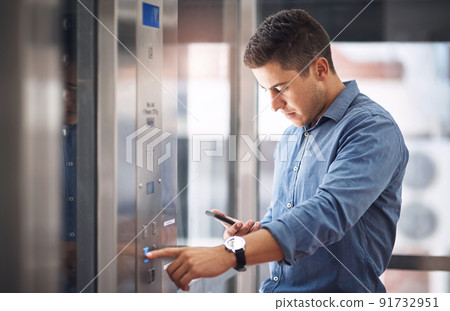 Hes heading straight to the top. Shot of a young businessman using a cellphone while pushing a button in an elevator. 91732951