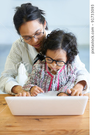 Following in mommy's footsteps. A cute little girl sitting on her mother's lap while working on the computer. Following in mommy's footsteps. A cute little girl sitting on her mother's lap while working on the computer. 91733093