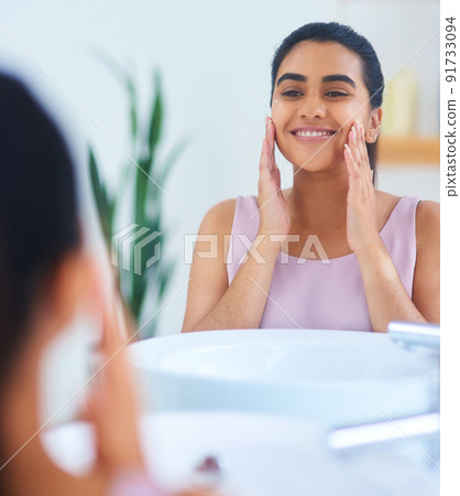 Not a single blemish in sight. Shot of a young woman applying moisturiser to her face in a bathroom at home. Not a single blemish in sight. Shot of a young woman applying moisturiser to her face in a bathroom at home. 91733094