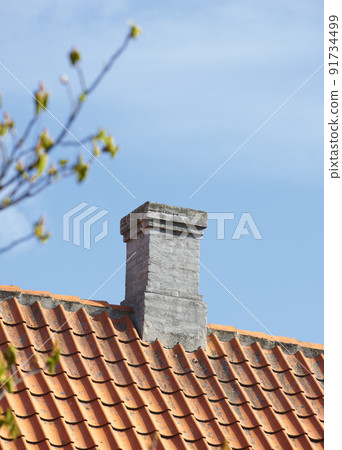 Grey brick chimney designed on slate roof of house building outside against blue sky background. Construction of exterior architecture of escape chute built on rooftop for fireplace smoke and heat Grey brick chimney designed on slate roof of house building outside against blue sky background. Construction of exterior architecture of escape chute built on rooftop for fireplace smoke and heat 91734499