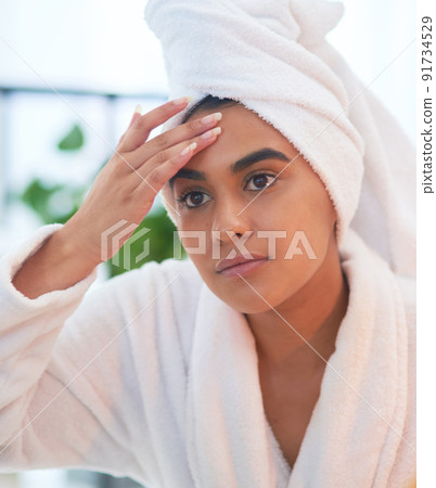 Should I be worried about wrinkles too. Shot of a young woman looking at her face in a bathroom mirror at home. 91734529