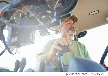 Working the fields. Shot of a farmer working inside the cab of a modern tractor. 91735300