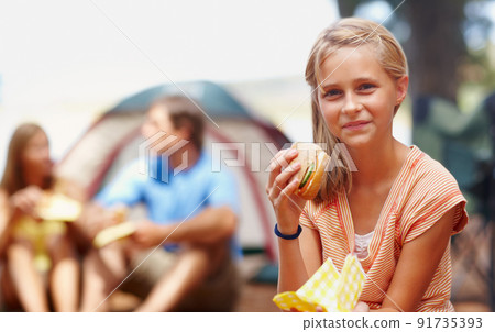 Cute girl eating burger. Portrait of cute young girl eating burger while on a camping holiday with family. Cute girl eating burger. Portrait of cute young girl eating burger while on a camping holiday with family. 91735393