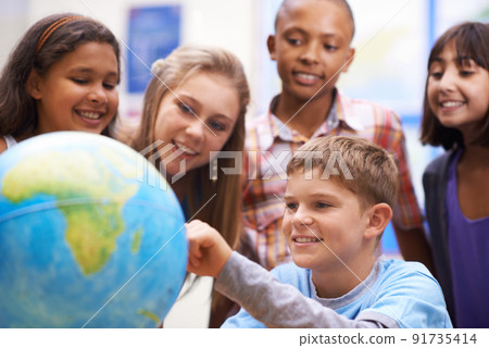 Here it is - Geography class. A group of pupils looking at a globe during geography class. 91735414