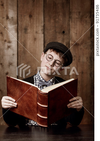 Learning lots of new things. Young boy in retro clothing wearing spectacles reading a massive book thooughtfully. 91735486
