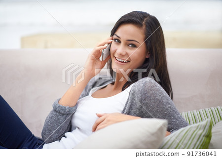 Catching up over the phone. Shot of a young woman sitting on a sofa and talking on the phone. 91736041