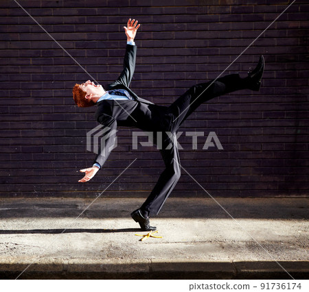 Theres no avoiding the banana skins in business. A young businessman tripping on a banana peel. 91736174