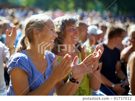 Enjoying the festival vibe. Two mature woman sitting outdoors at a music festival. Enjoying the festival vibe. Two mature woman sitting outdoors at a music festival. 91737012