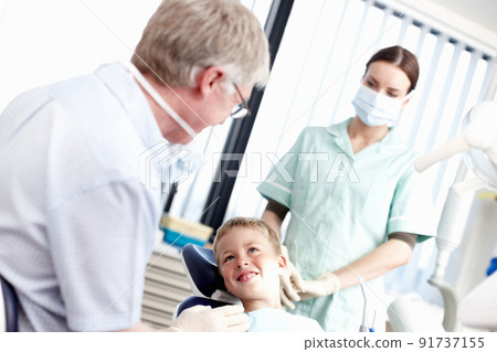 Dental treatment clinic. Portrait of young boy smiling at dentist with assistant in office. 91737155