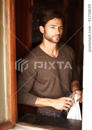 Long night ahead. Shot of a handsome young man drying off a glass while looking through a window. Long night ahead. Shot of a handsome young man drying off a glass while looking through a window. 91738639