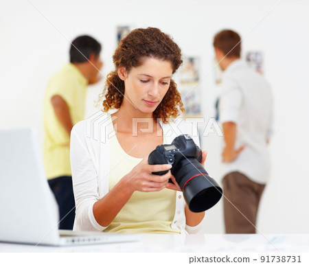 Woman checking out images in camera. Female photographer checking out images in camera with colleagues in background. 91738731