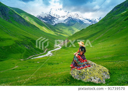 Tourist sitting on the rock at green pasture against highest georgian mountain Shkhara near Ushguli in Georgia. Tourist sitting on the rock at green pasture against highest georgian mountain Shkhara near Ushguli in Georgia. 91739570