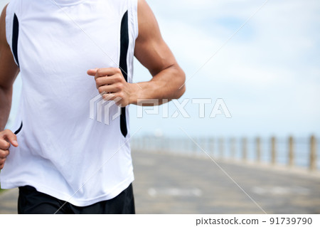 Push your body beyond its limits. Cropped image of a fit and athletic male running on a beach promenade outside - copyspace. 91739790
