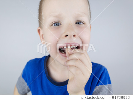 Loose baby teeth. Blond boy touches a milk tooth with his hands and shows how he moves. Stages of growing up. Loose baby teeth. Blond boy touches a milk tooth with his hands and shows how he moves. Stages of growing up. 91739933