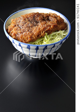 A hot sauce and bowl with a cutlet entwined with plenty of sauce on top of shredded cabbage shot on a black background 91740141