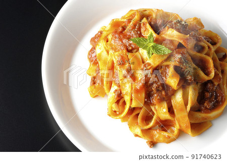 A bird's-eye view of the hot Bolognese, which is often entwined with flat pasta fitcine and tomato sauce, on a black background. 91740623
