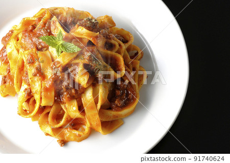 A bird's-eye view of the hot Bolognese, which is often entwined with flat pasta fitcine and tomato sauce, on a black background. 91740624
