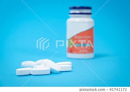 A jar of dietary supplements and white pills on a blue background, a place for text. Vitamins and trace elements for a complete diet 91741172