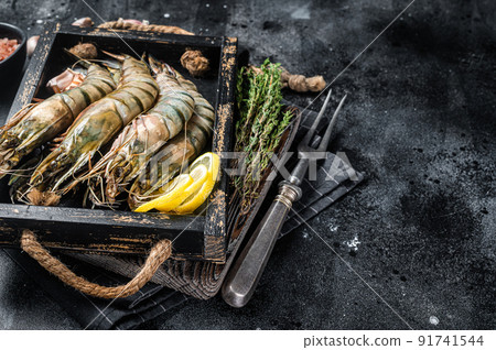 Raw fresh Giant Black tiger prawns shrimps in a tray with lemon and thyme. Black background. Top view. Free copy space Raw fresh Giant Black tiger prawns shrimps in a tray with lemon and thyme. Black background. Top view. Free copy space 91741544