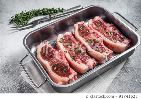 Marinated Raw meat of lamb mutton saddle in steel tray with thyme, spices and olive oil. White background. Top view 91741623