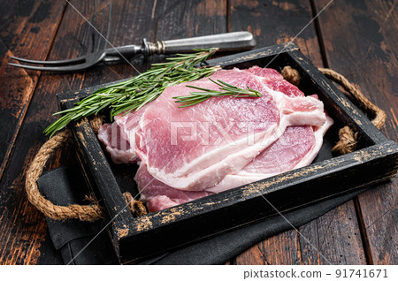 Ready for cooking raw pork chop steaks in a wooden tray with rosemary. Wooden background. Top view 91741671