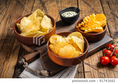 Variety of Potato chips - Crinkle, homemade, hot BBQ. Wooden background. Top view Variety of Potato chips - Crinkle, homemade, hot BBQ. Wooden background. Top view 91741682