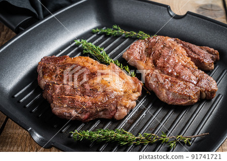 Grilled Chuck eye Roll beef steaks with herbs on grill skillet. Wooden background. Top view Grilled Chuck eye Roll beef steaks with herbs on grill skillet. Wooden background. Top view 91741721